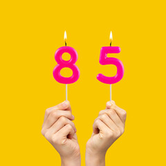 Hands holding birthday candles with number 85 - Yellow background