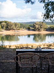 Fototapeta premium Outdoor dining setup by a calm lake with distant trees and clouds