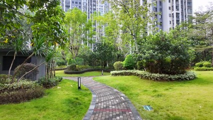 A curved brick pathway winds through a lush communal garden surrounded by modern apartment towers in China. A public outdoor area or urban oasis blending nature with contemporary residential living.