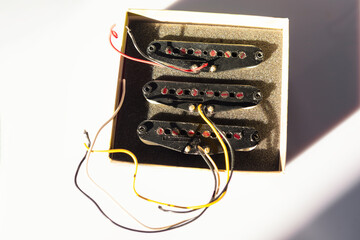 Three black single-coil guitar pickups with red pole pieces sit in a foam-lined box, casting...
