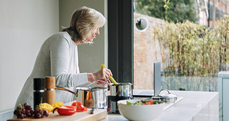 Laptop, cooking and senior woman in the kitchen of modern home for healthy or diet supper. Food, technology and elderly female person preparing a meal for dinner or lunch with computer at house.