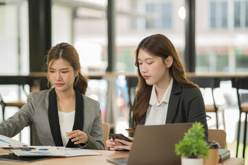 Two businesswoman sitting and working together checking documents in the office with her female friend.