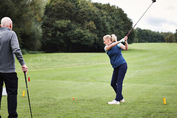 Obraz premium Woman, golf course and swing club on field for training, contest or sport in summer with fitness. Girl, athlete and people with outdoor games for workout, wellness and exercise on grass in Scotland
