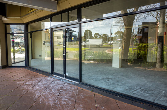 Empty commercial storefront with large glass windows and doors reflecting the corner street view, showcasing a vacant interior space ready for new business development or available for lease.