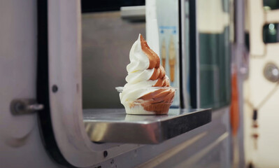 Swirled vanilla and chocolate soft serve ice cream in a cup, freshly served from a food truck window, capturing a nostalgic summer treat moment.