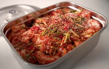 Freshly prepared Korean kimchi stored in a stainless steel container, topped with sesame seeds and green onions, showcasing a vibrant and spicy traditional dish.