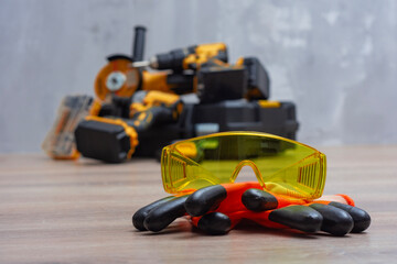Close-up of yellow safety goggles and work gloves, with a cordless tool kit in the background....