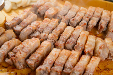 Bite-sized pieces of pork belly being grilled on a yellow pan
