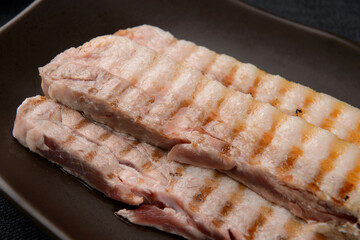 Grilled pork belly on a black plate
