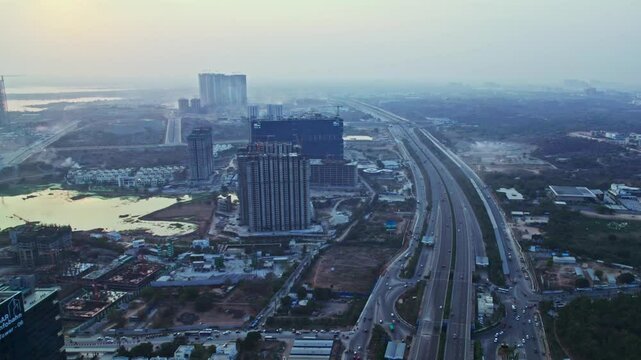 Hyderabad outer ring road with lake and under construction buildings, at day time, push in, tilt down, drone shot, 4k.