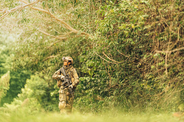 Wearing full camouflage gear and a tactical helmet, the soldier carefully scans the area through...
