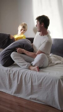 Father and son fooling around at home on a bed on weekend. Happy parent with hyperactive child. Single father