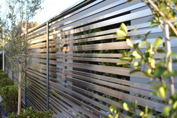 Obraz premium Modern minimalist zen garden featuring a brushed stainless steel horizontal slat fence and clean contemporary home architecture.