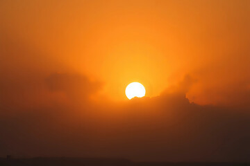 Orange sky with sun and clouds during hot summer weather.