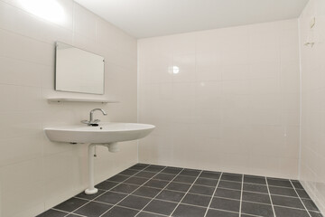 A clean and minimalist bathroom featuring a wall-mounted sink, a square mirror, and tiled flooring, creating a spacious and modern aesthetic.