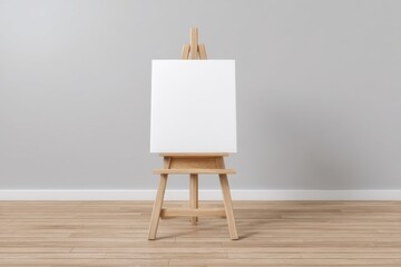 Blank canvas on wooden easel in minimalistic studio interior with light wood flooring and gray walls