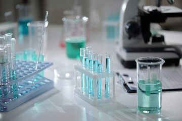 Laboratory tabletop with various beakers, test tubes, and a microscope in focus. Presence of chemical solutions in containers, indicative of ongoing experiments