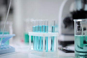 Laboratory equipment with several test tubes filled with a vibrant blue liquid. Beaker in the background along with a pipette can be seen, indicating a scientific experiment setting