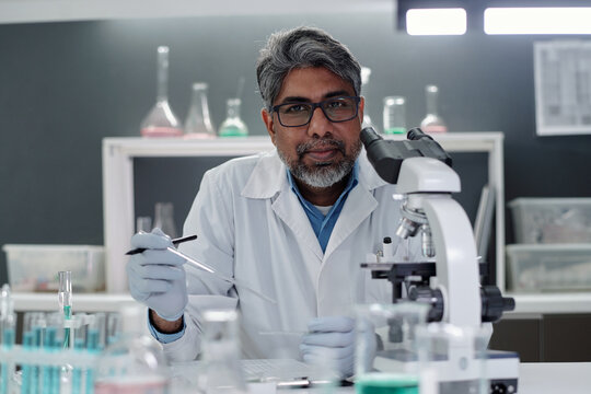 Portrait of scientist examining samples with precision equipment in modern laboratory. Senior researcher concentrating on experimental procedures while wearing lab coat and glasses