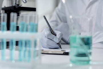 Gloved hand holding pen, interacting with papers, surrounded by laboratory equipment, blue...