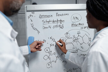 Two scientists analyzing intricate chemical reactions on whiteboard, discussing molecular formulas...