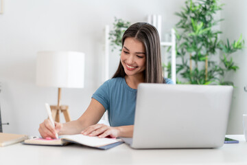 Asian attractive woman taking notes on book while learning from home.