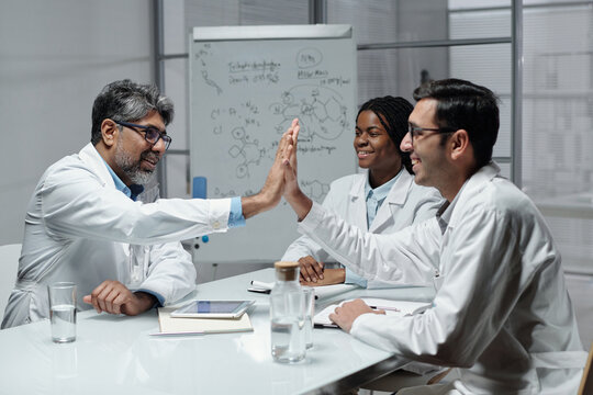 Group of scientists discussing research findings in laboratory setting with whiteboard in background and glass of water on table. Engaging and collaborative environment