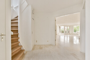 A spacious and modern interior featuring light-colored walls and flooring, a staircase, and large windows that provide ample natural light.