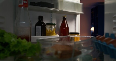 The man opens the refrigerator and takes a bottle of beer from the shelf. Evening leisure. View from the refrigerator