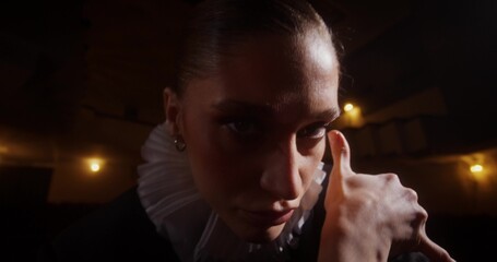 Close-up of a woman's face with a frill around her neck dancing standing between chairs in an empty...