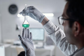Scientist holding flask with green liquid while meticulously observing analysis in laboratory....