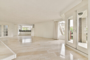 An expansive modern living area flooded with natural light, featuring elegant marble flooring and large glass doors leading to a balcony.
