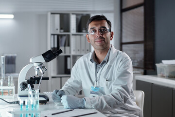Scientist wearing lab coat and safety glasses examining samples with microscope in modern laboratory setting showing concentration and dedication to scientific research