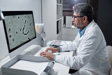 Scientist observing microscopic sample on computer screen in laboratory filled with medical...