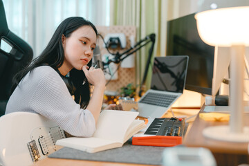 Young woman composer playing electric guitar music with digital technology at home studio