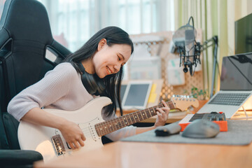 Young woman composer playing electric guitar music with digital technology at home studio