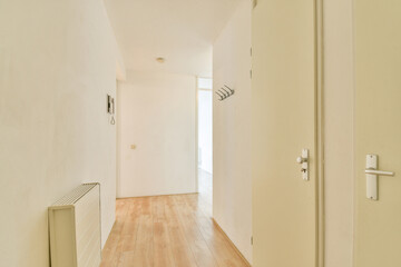A spacious and well-lit hallway featuring clean lines, light wooden flooring, and subtle wall...