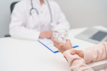 Senior woman with Tremor hand during taking glass of water in hospital. Parkinson disease April...