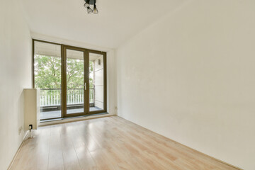 An empty room featuring wooden flooring and large windows, letting in abundant natural light. The clean lines and neutral colors create a serene atmosphere.