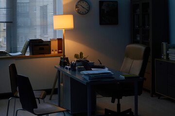 Dark office of school psychologist with armchair standing by his workplace with laptop, green plants and stack of documents