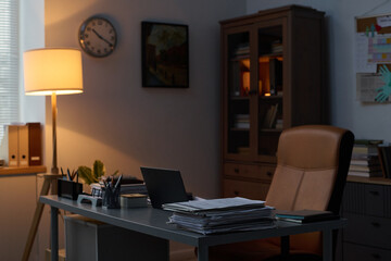 Workplace of modern psychologist with armchair standing by desk with stack of paper documents, laptop, notepads and pens