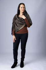 A  dark-haired woman wearing black pants, a brown top and a woven paisley shawl draped over her...