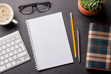 Top view of a dark leather office desk with notepad, supplies, and coffee cup