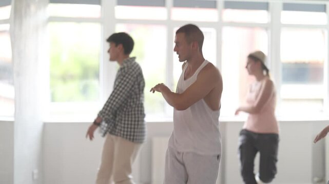 Young man standing performs basic hip hop movements in front of group of students. Developing precise movements, rehearsing arc elements, nae nae moving 