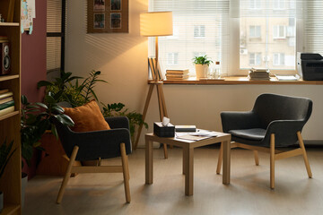 Small square table with box of tissues, paper documents and notepad of psychologist standing...