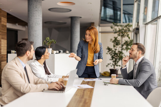 Female chief standing at boardroom at corporate firm and discussing project with her employees.