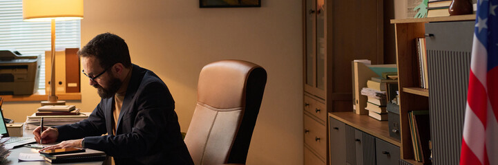 Header of mature school psychologist sitting in armchair and bending over workplace while taking...