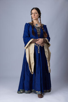 A Medieval woman wearing a blue silk gown called a bliaut. She has long, dark hair arranged into plaits. 