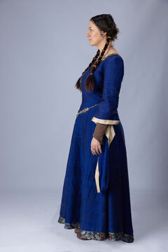 A Medieval woman wearing a blue silk gown called a bliaut. She has long, dark hair arranged into plaits. 