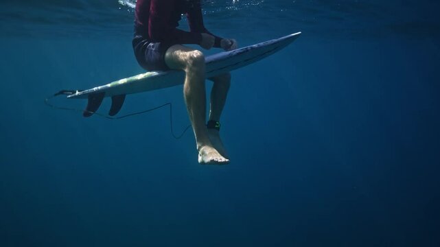 Underwater view of surfer sitting on surf board in tropical clear blue ocean